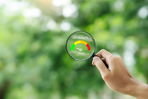 A hand holding a magnifying glass with a graphic depicting an air quality meter inside of it over a green blurry background