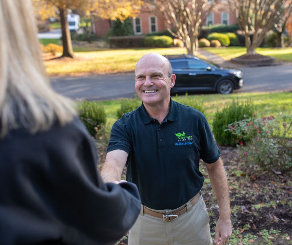 man in black polo shaking woman's hand in front of her home