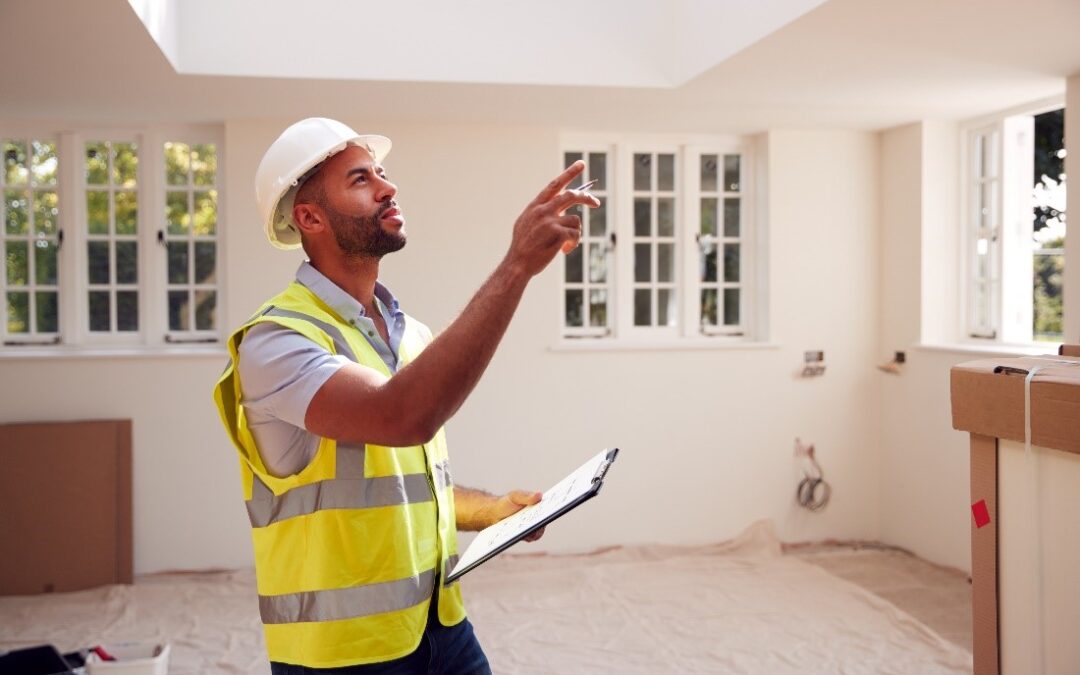 A Man in a Safety Vest and a Hard Hat Holds a Clipboard and Points at Something with a Pen During an Inspection