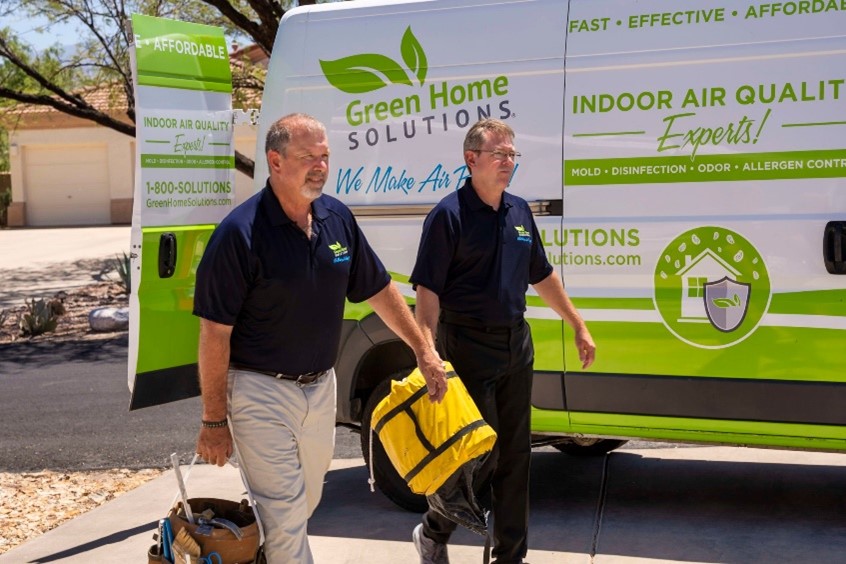 Two men in branded Green Home Solutions uniforms walk beside a branded truck with a yellow work bag.