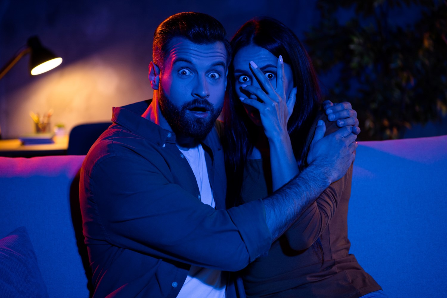 A Man with a Starled Expression Embraces a Scared Woman with Her Hand Over Her Face Peeking Through Her Eyes