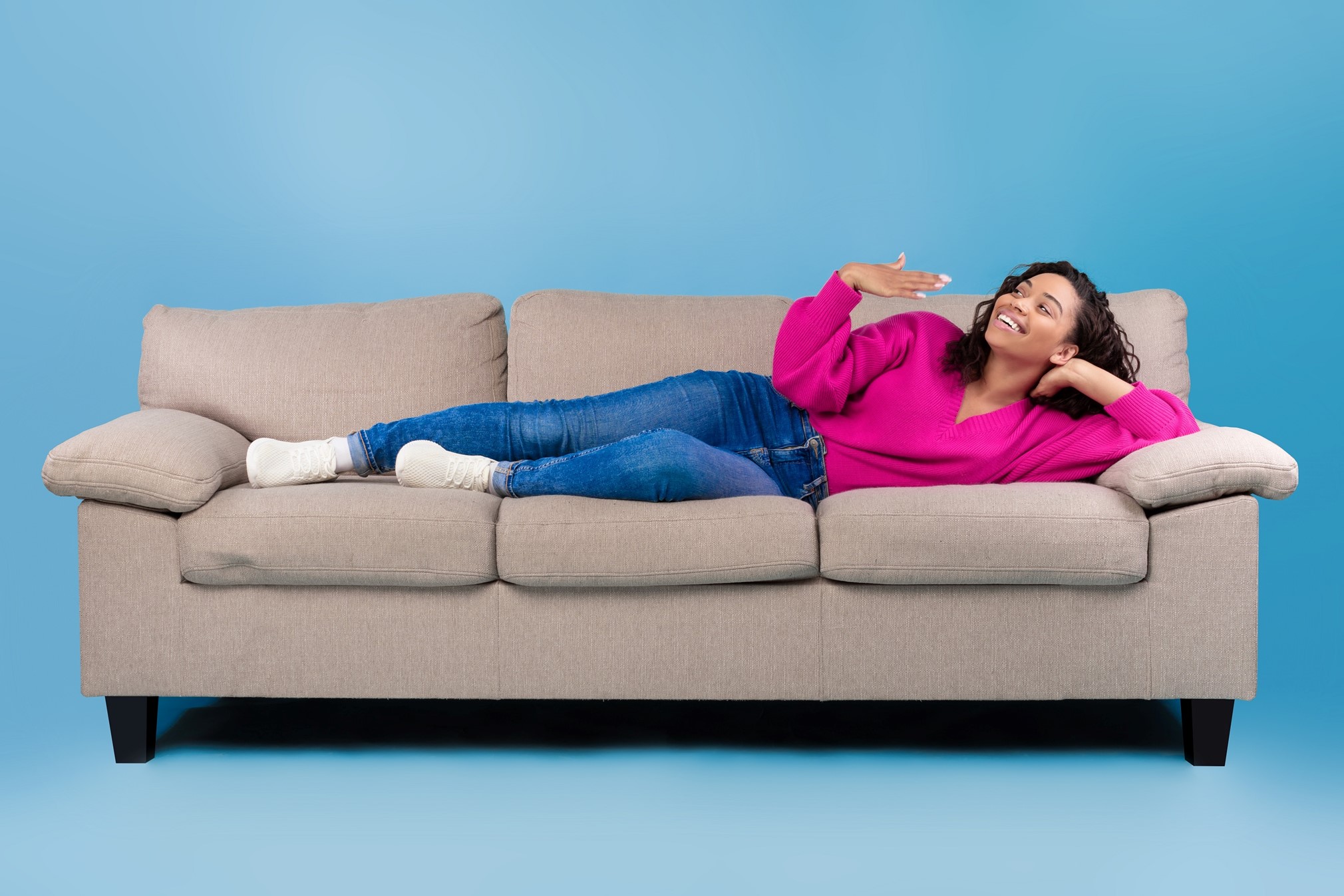 A smiling woman lies on a couch fanning herself as if to show she is moving cool air from her air conditioner towards her