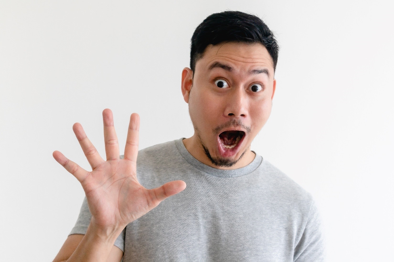 A man holding up his hand, showing all five fingers with an excited expression on his face. 