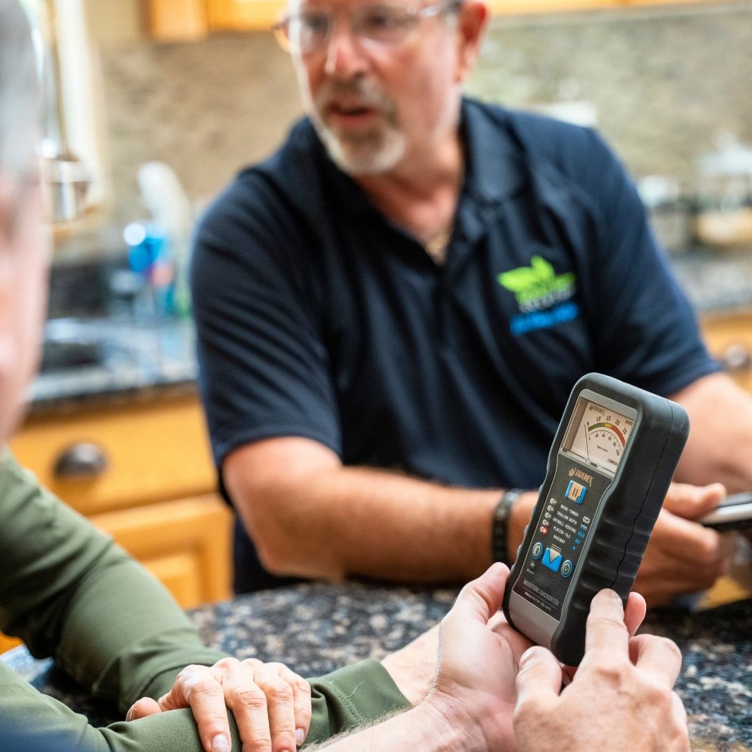 man in black polo with woman looking at indoor air quality testing meter